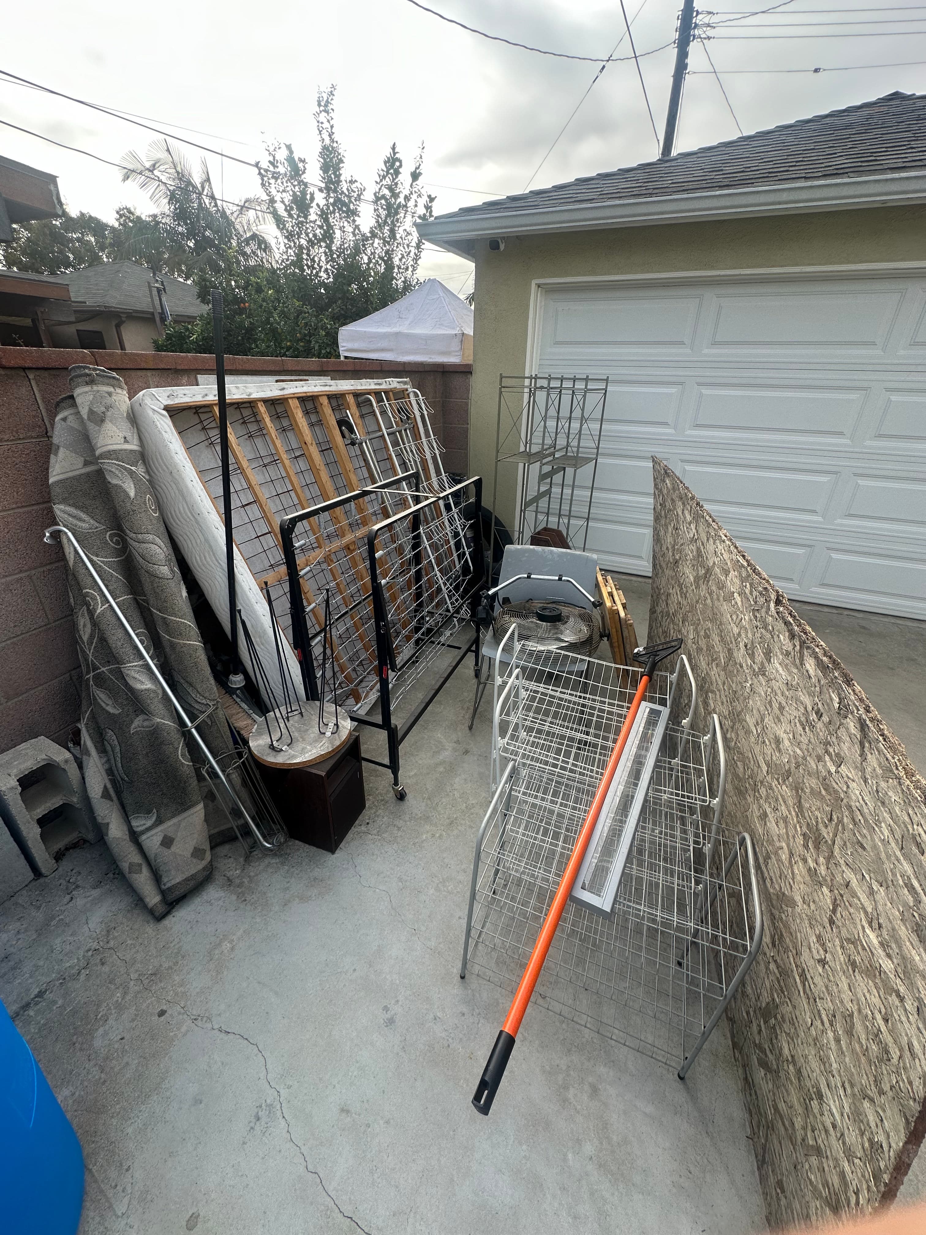 Piled discarded furniture and metal racks in a residential outdoor space.