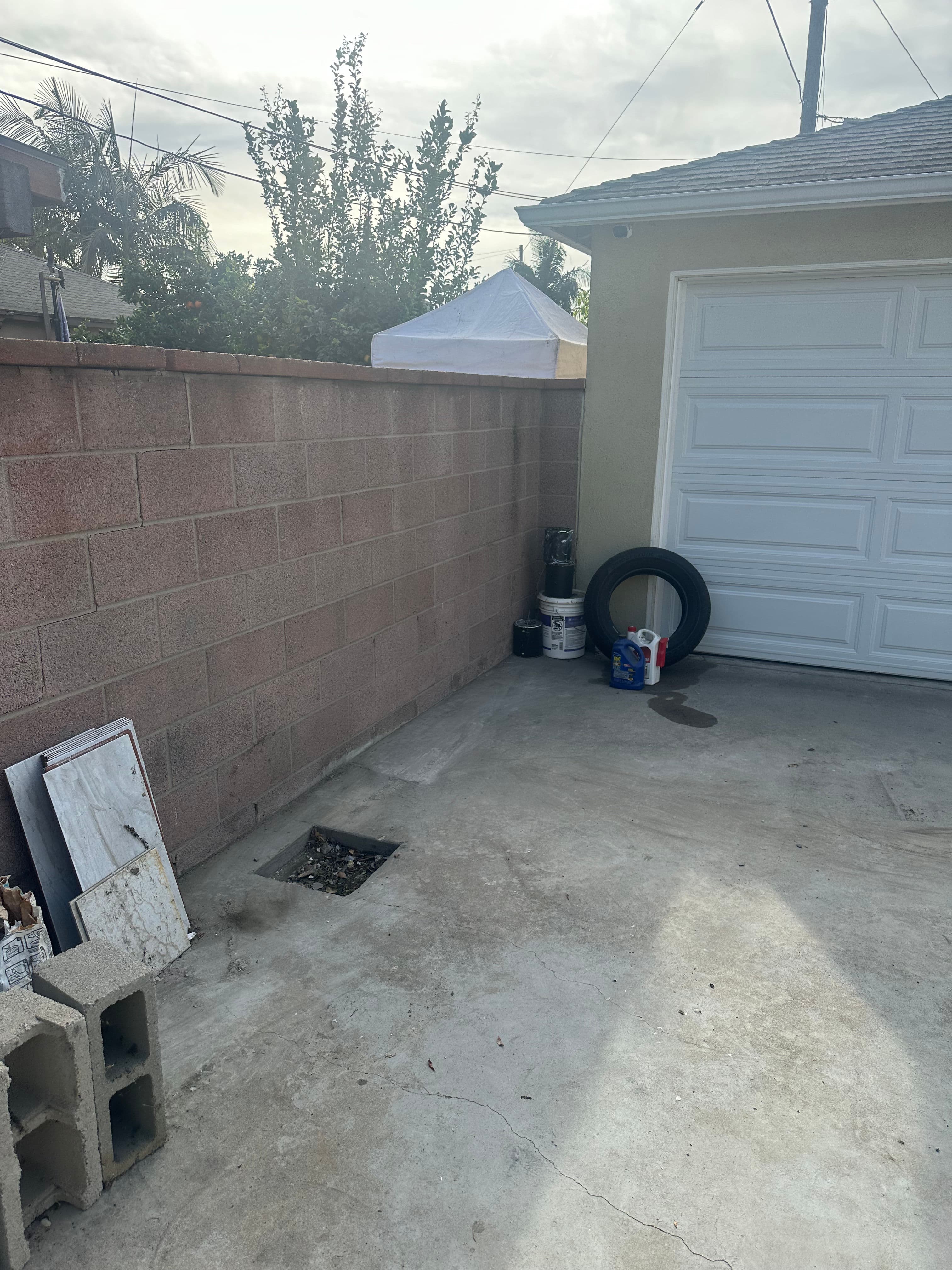 Empty garage area with cinder block wall, tire, and paint cans under a cloudy sky.