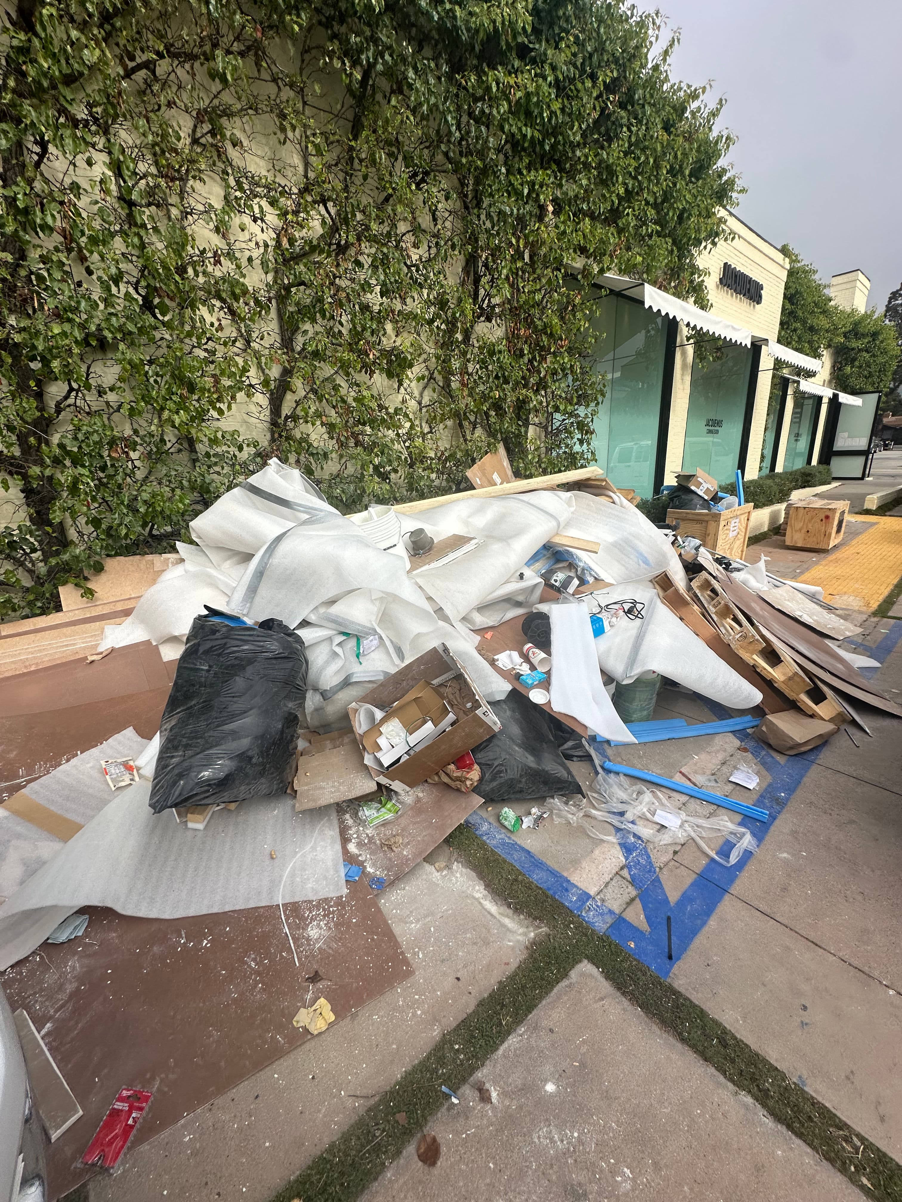 pile of mixed debris and trash on sidewalk next to a building surrounded by greenery