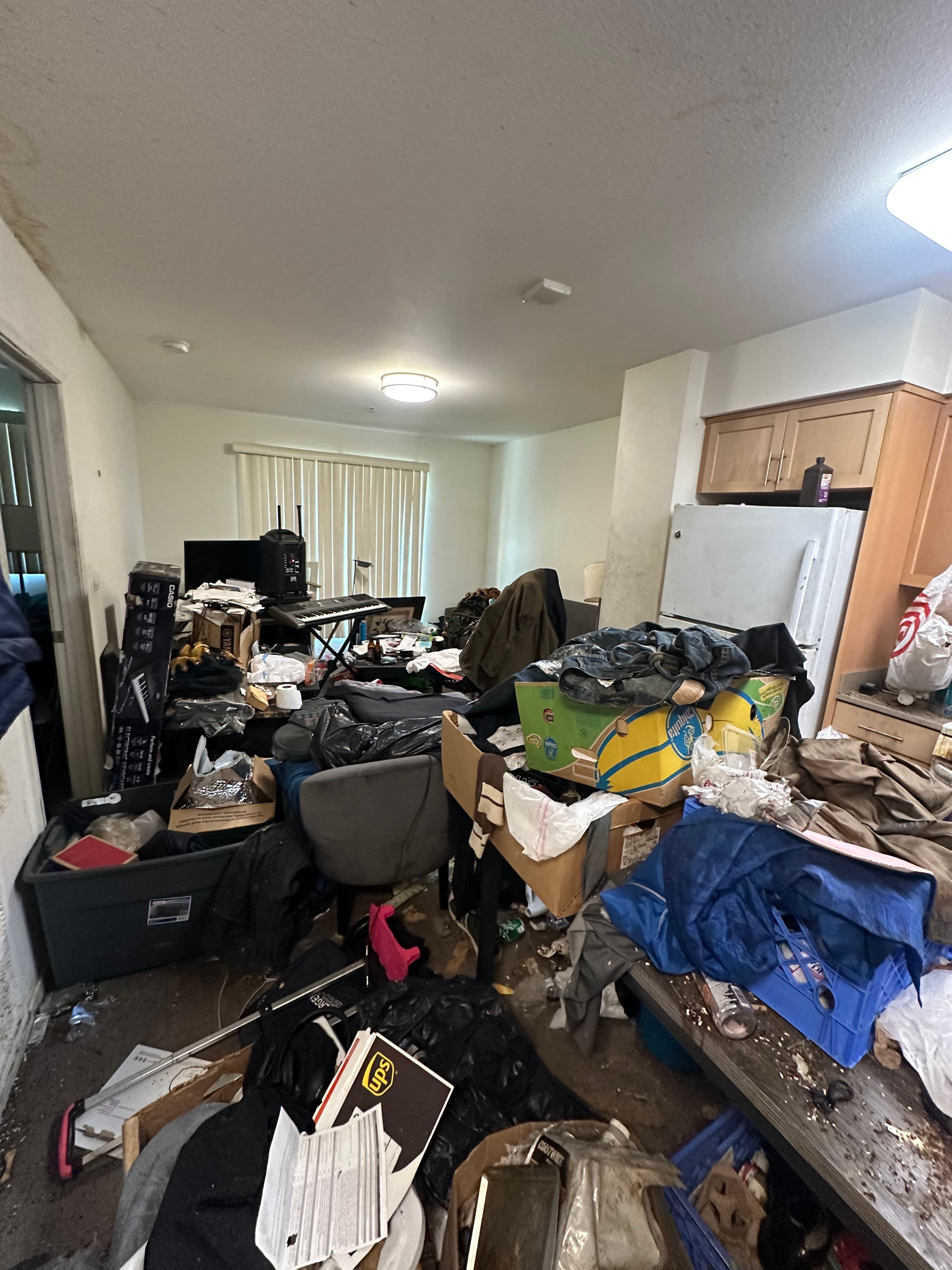 Cluttered living space with piles of trash, boxes, and disorganized furniture in disarray.