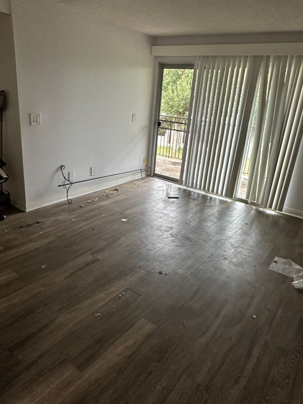 Empty living room with wooden floors and sliding glass door, sunlight streaming through.