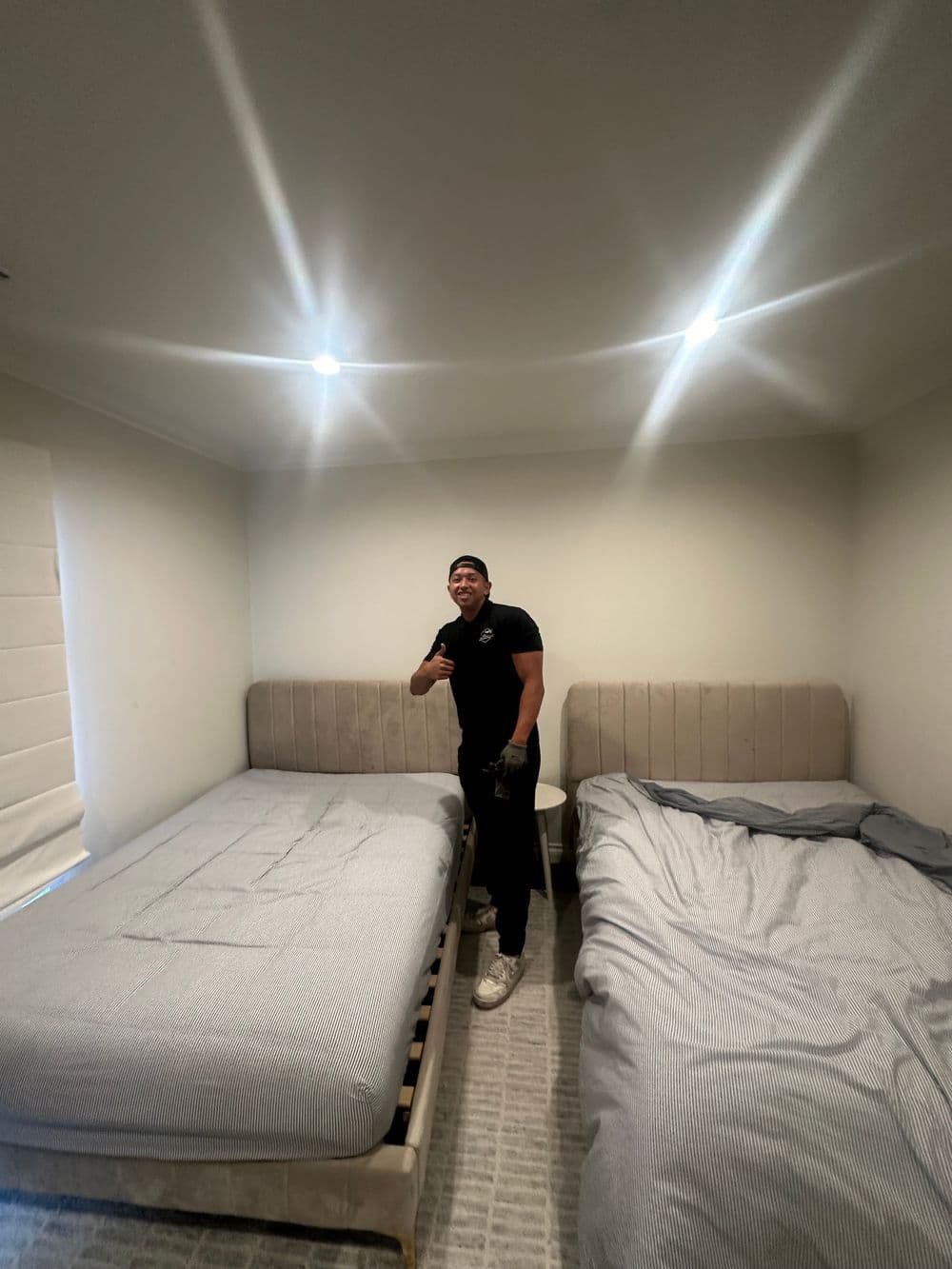 Man posing in a well-lit bedroom with two beds and modern decor.
