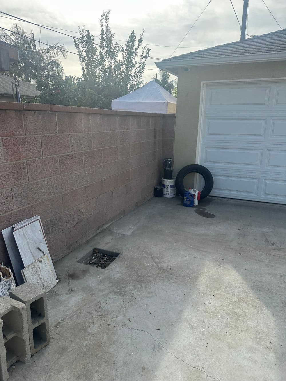 Concrete yard area beside garage with tire, paint cans, and cinder blocks against a wall.