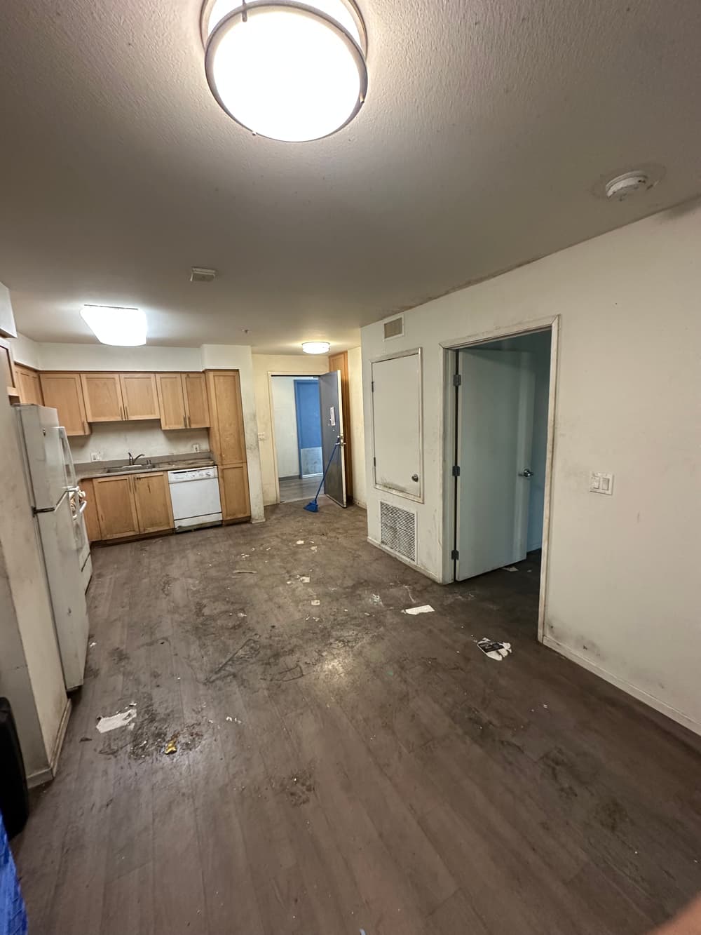 Abandoned dirty apartment interior with kitchen, stained floors, and cluttered space.