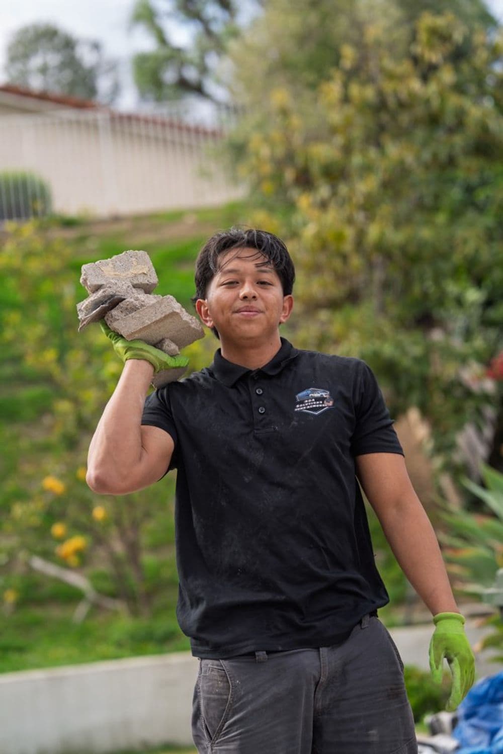 Man in black shirt carrying bricks outdoors in a green landscape. Labor work in construction.
