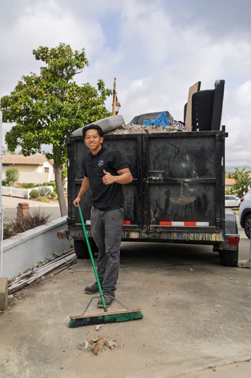 Man sweeping debris near a truck filled with junk outside a residential area.