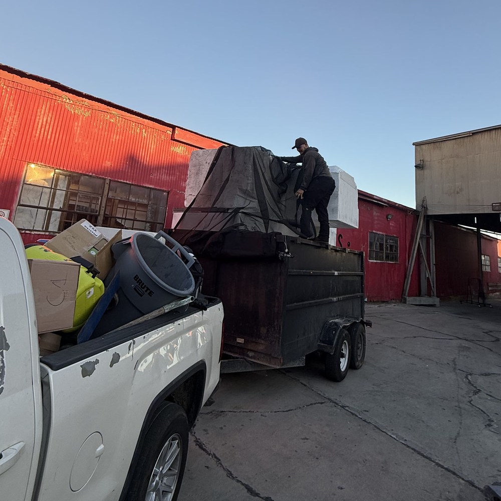 Roa Solution crew member strapping down a loaded dump trailer behind the pickup