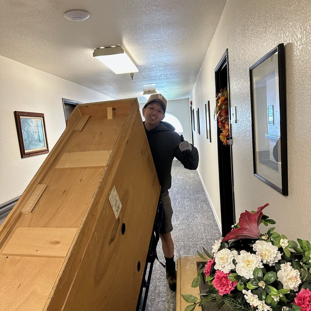 Crew member carrying a large wooden cabinet out of a house