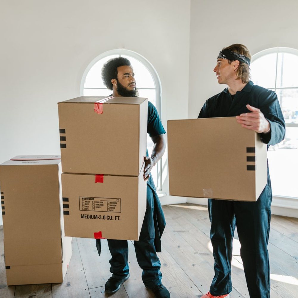 Two movers carrying cardboard boxes out of an emptied room