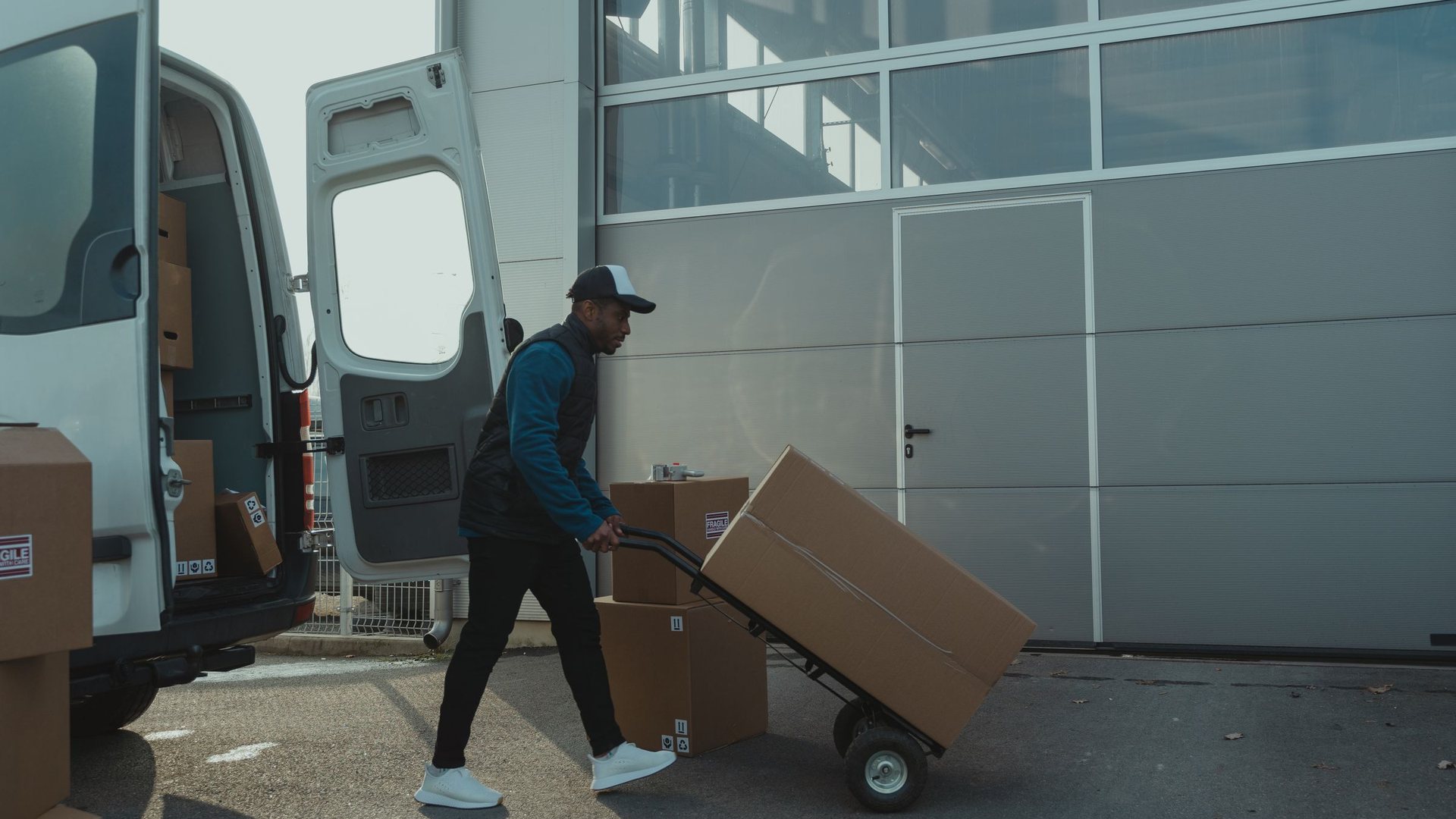 Worker moving boxes on a hand truck toward a van in Garden Grove