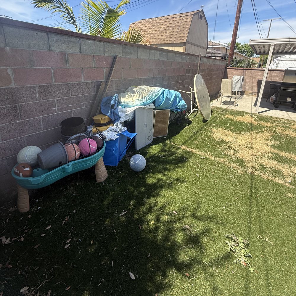 Old toys, chairs and outdoor junk piled along a backyard wall